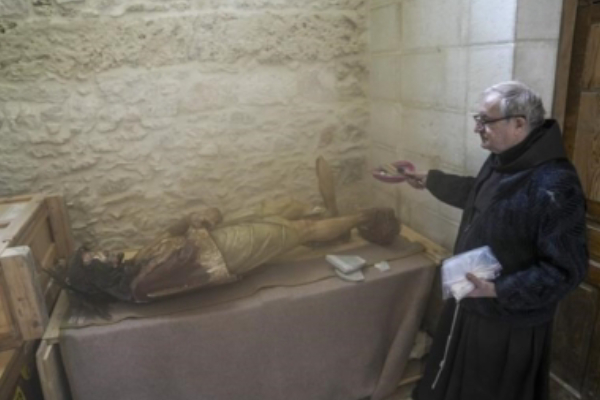 A priest stands by a damaged statue